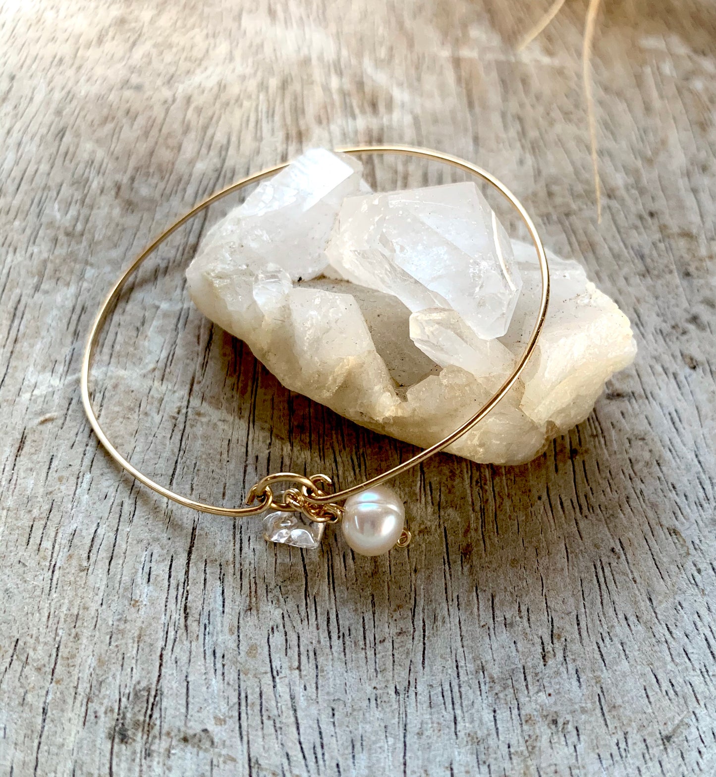 Esther pearl & clear quartz petite bangle, gold pearl bangle, full view single bangle on crystal and wooden surface